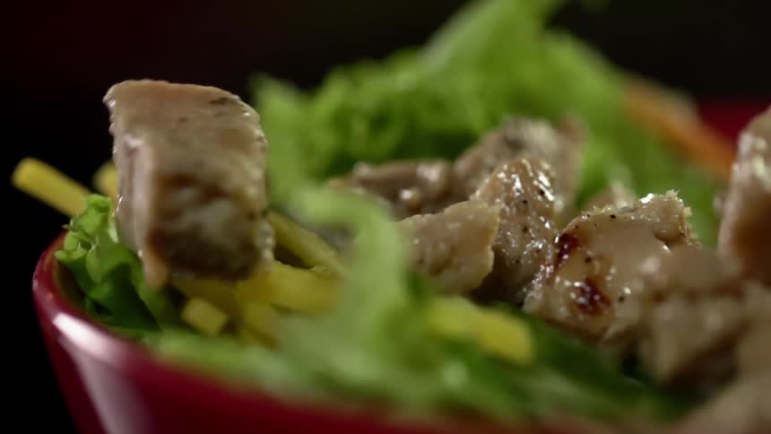 Diced pork falling inside a red ceramic bowl filled with leafy greens salad