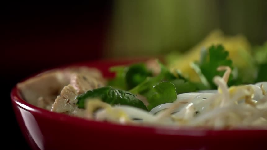 Green herbs drop into a bowl filled with food