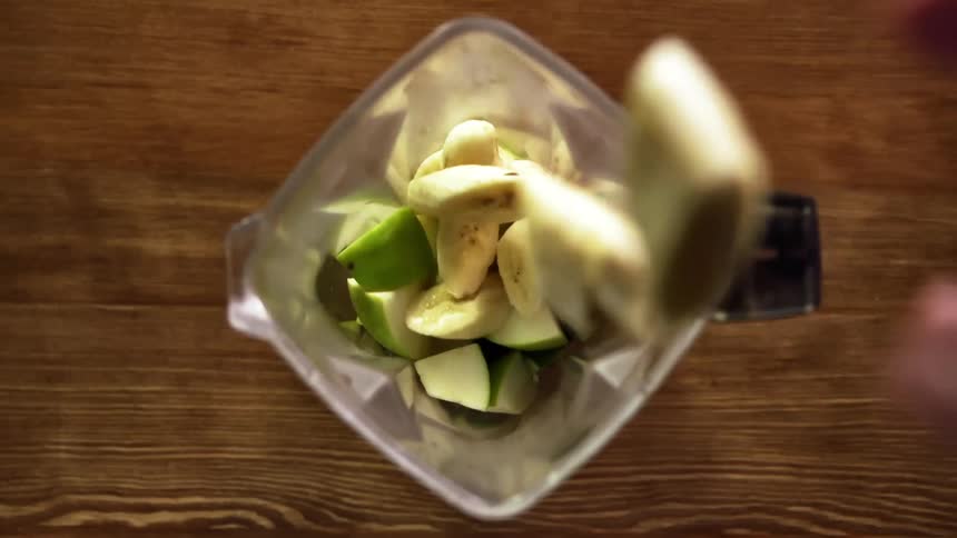 A person puts apples and bananas in a blender