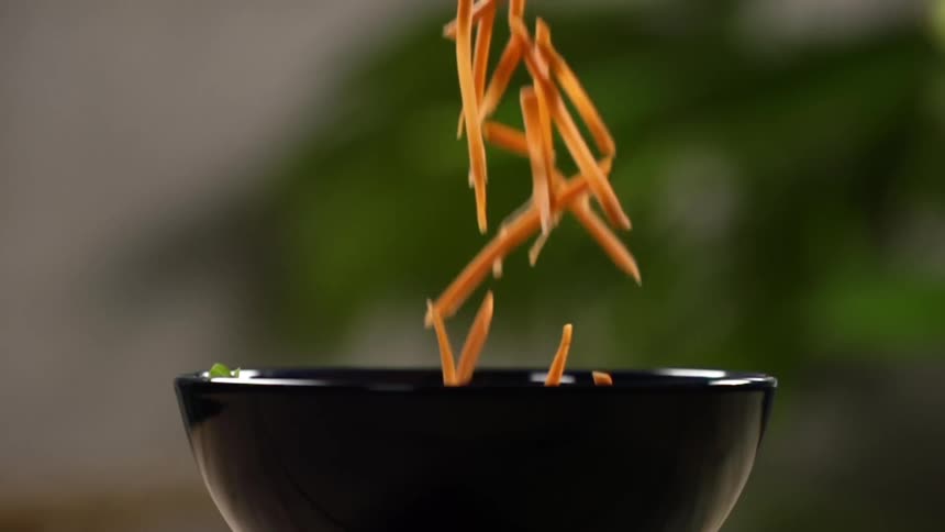 Shredded carrots are dropped into a small black bowl