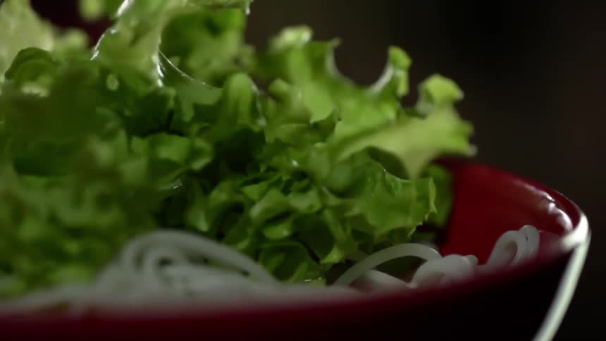 Leafy green vegetables dropping over noodles in a red ceramic bowl