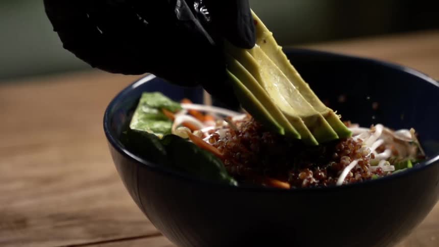 A cook places sliced avocado on top of a bowl of food