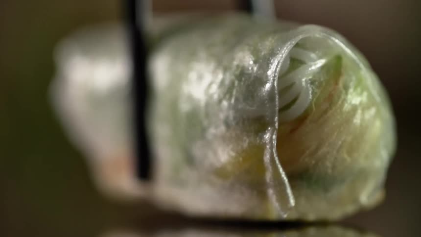 Metal tongs lower a piece of wrapped food