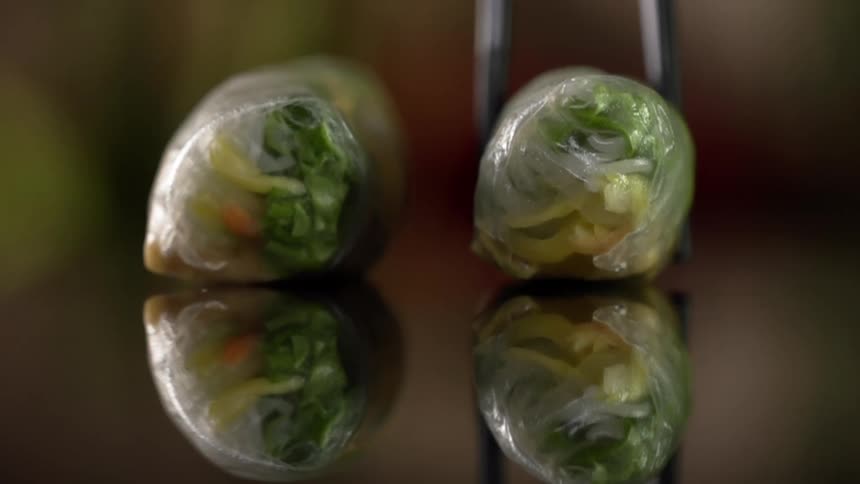 Vegetable sushi rolled in translucent wrapping placed with chopsticks over a reflecting surface
