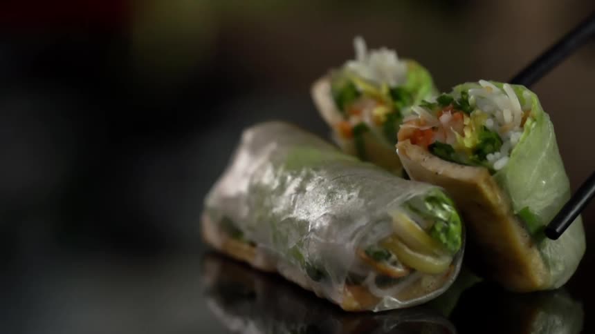 A cut half of a vegetable spring roll is carefully placed on its end next to an intact one