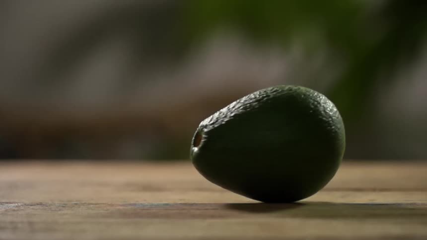 A single avocado is spinning on its side atop a wooden cutting board