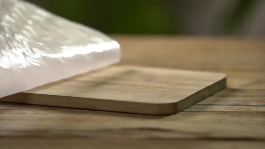 A round plastic mat is dropped on top of a wooden cutting board