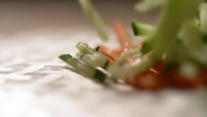 Thinly sliced cucumber falls onto a pile of carrot sticks