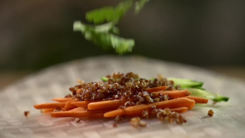 Herbs and spinach fall on top of quinoa and vegetables on a paper lined plate
