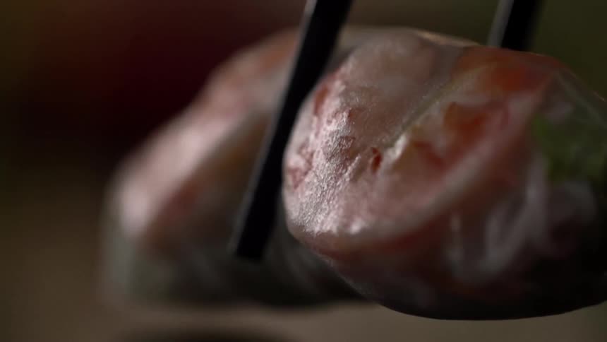 Translucent vegetarian wrap placed in a reflective surface using chopsticks