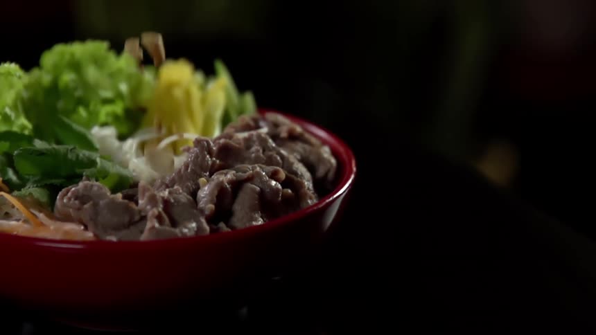 Peanuts falling on a dish of noodles filled with meat and vegetables