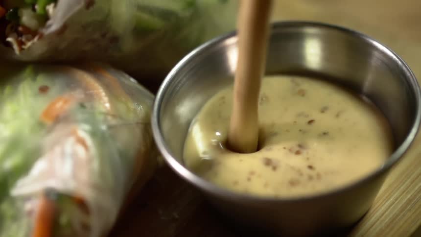 A dipping sauce for spring rolls is poured into a metal cup