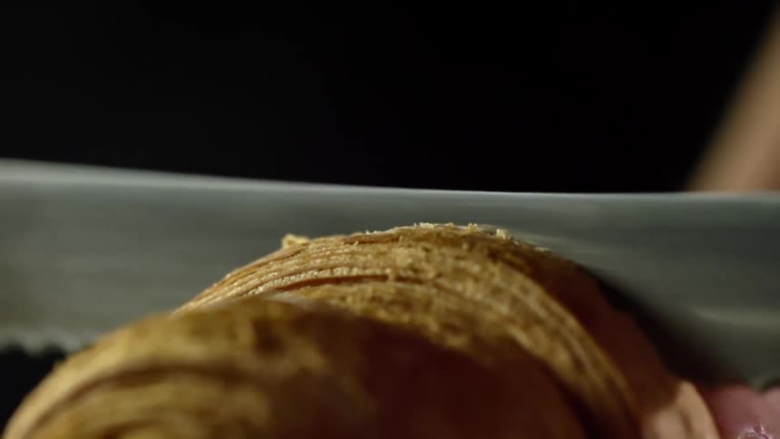 Close up of a bread knife cutting a croissant in half
