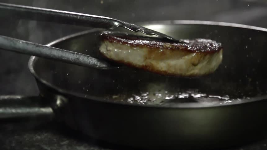 A piece of meat is lifted out of pan with oil sizzling in it
