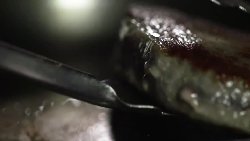 A piece of meat frying in a pan is removed
