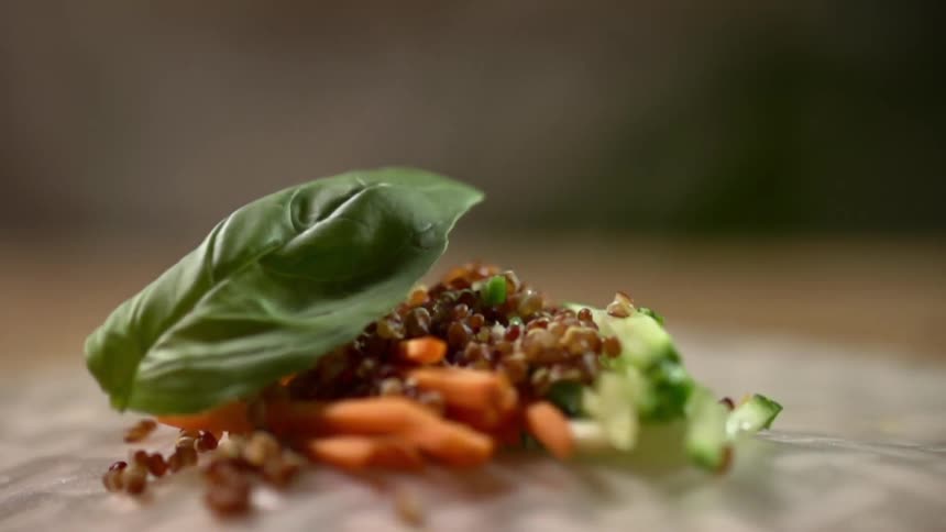 A spinach leaf falls on a plate of vegetables and quinoa