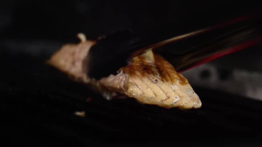 Tongs lift grilled fish fillet from grill surface