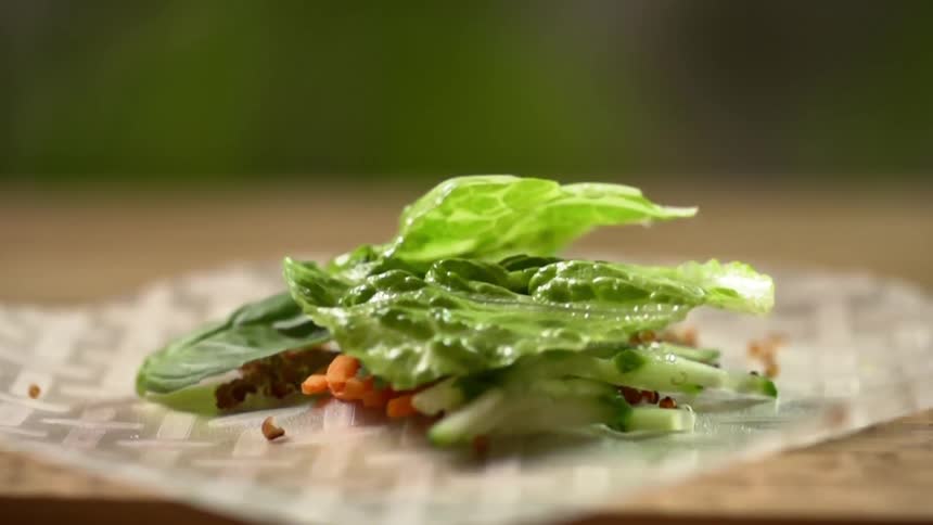 Green lettuce leafs fall over finely chopped vegetables over a translucent edible wrapper