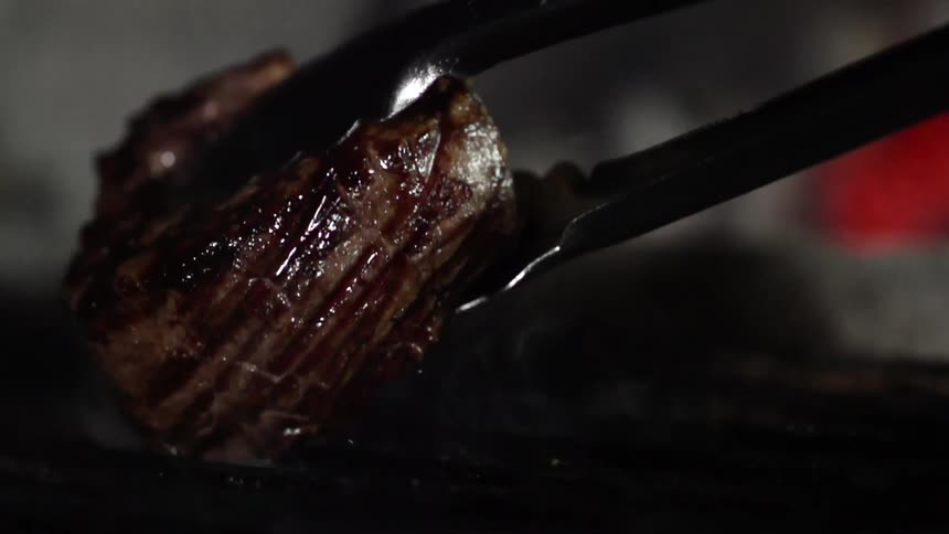 A pair of tongs lift a filet mignon off of a grill