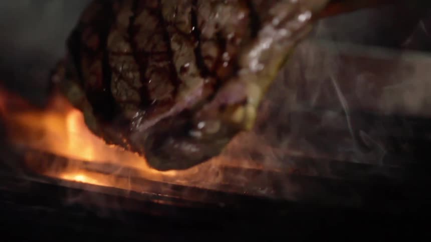 A grilling steak is lifted from the grill