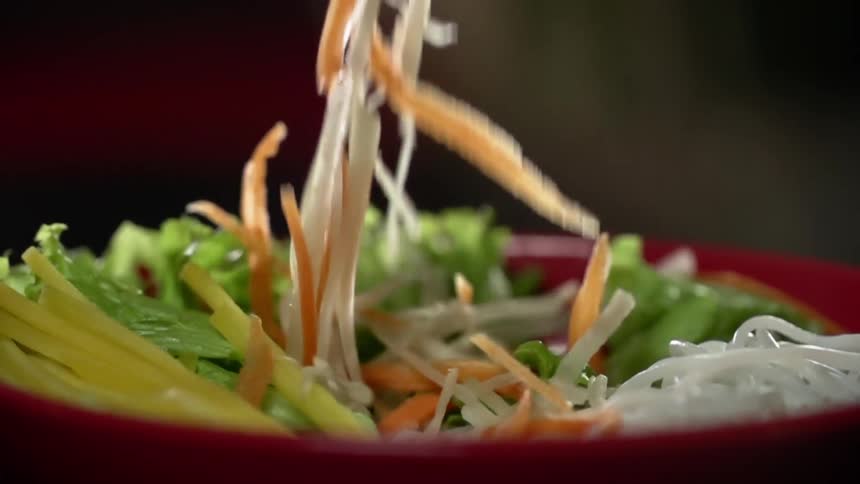 Sliced vegetables fall into a red bowl containing pasta and vegetables