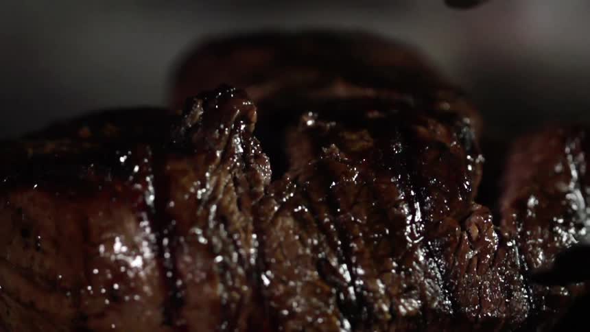 A grilled steak is placed on a black cutting board