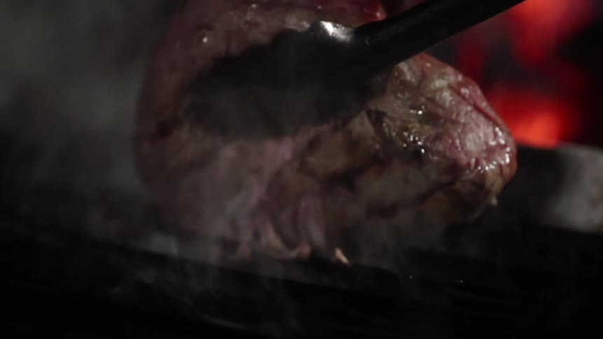 A steak is lifted from the barbeque