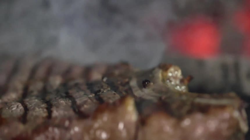 A partially cooked steak drops down onto a hot grill