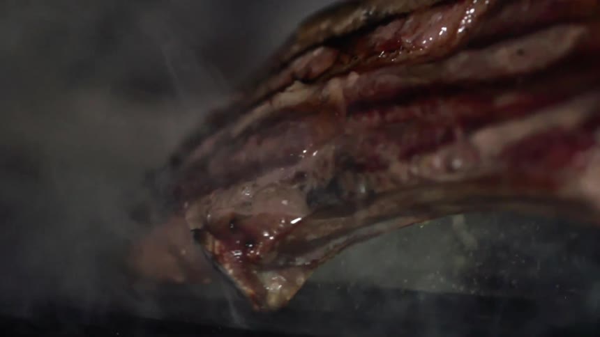 Tongs lift a steak off of a flame grill