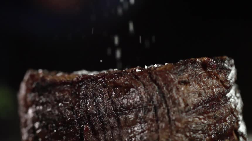 Juicy steak is added salt and stands out against the dark background