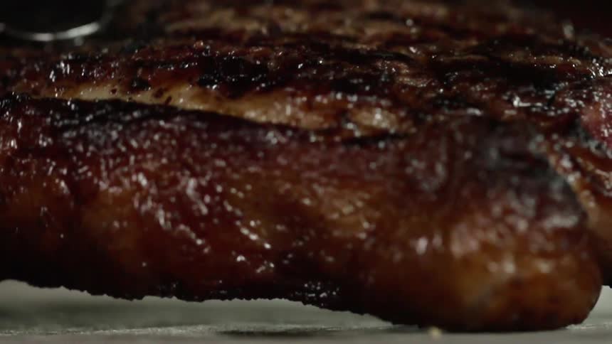 Tongs place cooked meat on a surface