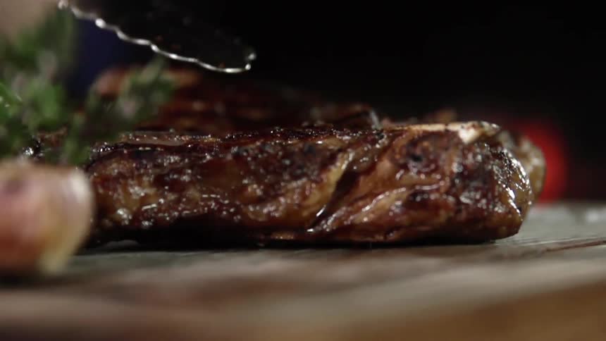 Close up of a grilled steak being put on a steak board by a pair of tongs