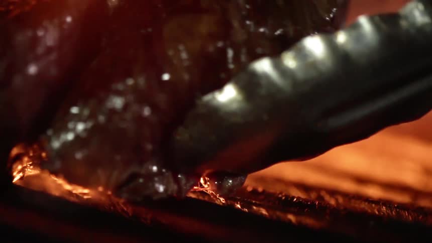 Meat being placed on a grill over open flames