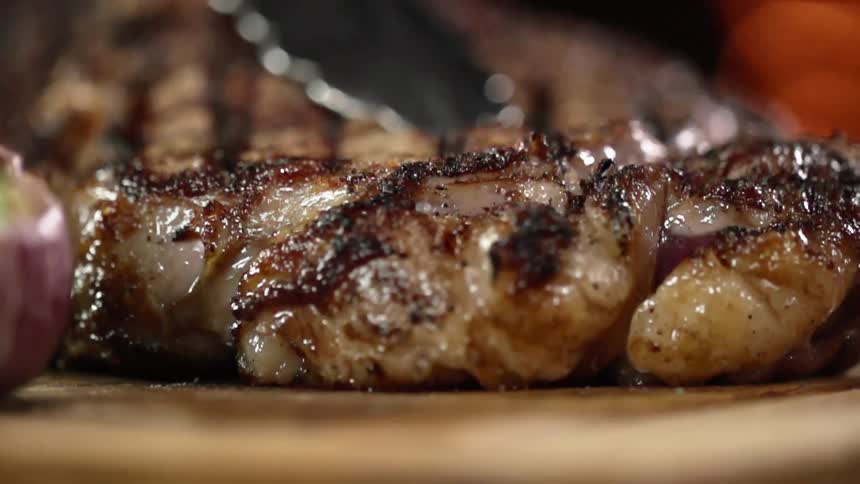 A steak with grill marks is placed on a board using tongs