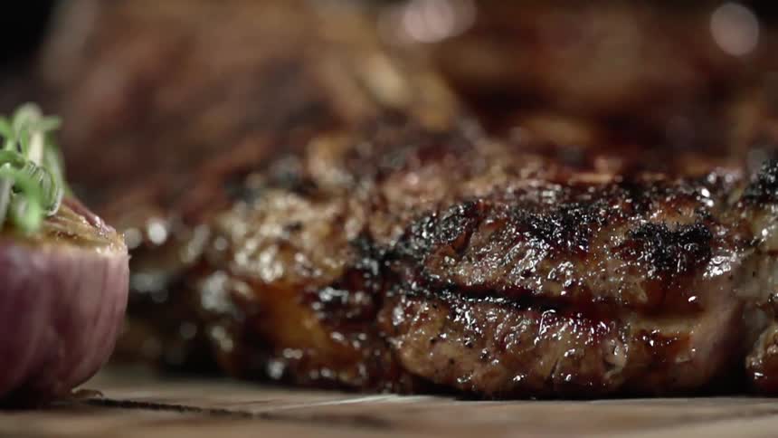 T bone steak being place over a wooden board with tongs