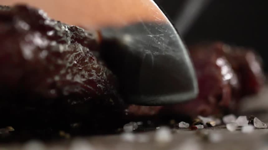 Close up of sharp knife slicing into a cooked piece of beef
