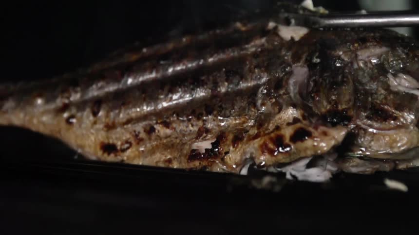 A cooked fish is flipped with tongs