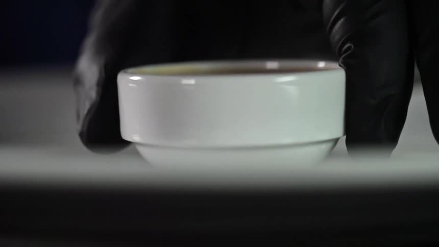 A person wearing black disposable gloves gently places a small white bowl onto a white plate