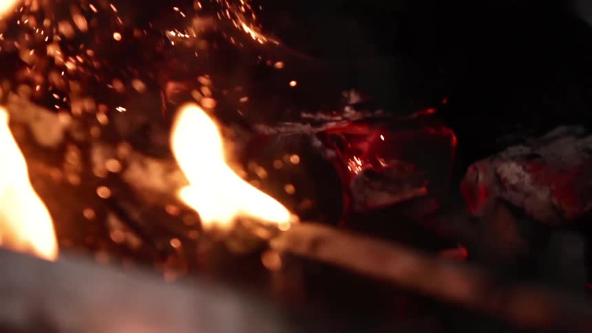 Shovel removing coals in a fire pit stirring up sparks and fire