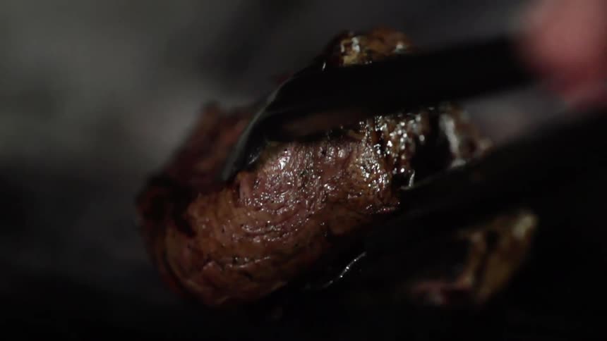 Grilled steak is picked up with metallic tongs