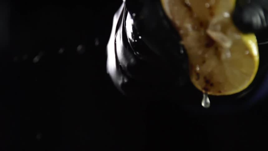 Close up of a hand with black glove squeezing a lemon