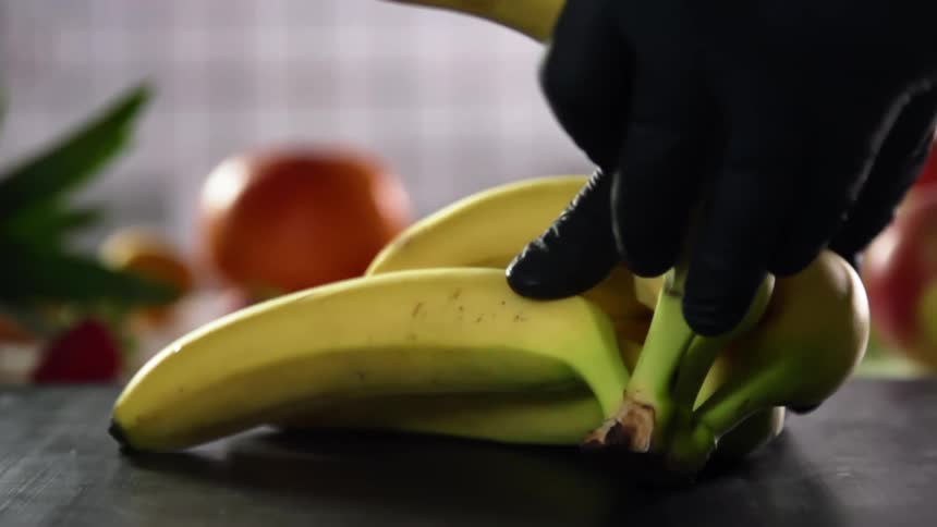 The cook with black gloves takes a banana from a bunch of bananas