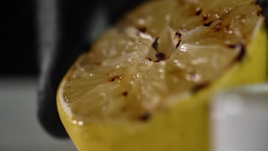 A person wearing a black glove sets a charred lemon on a table