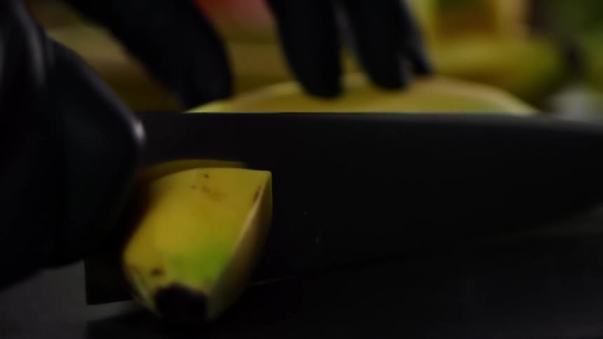 Close up of hands wearing black gloves cutting a long curved banana