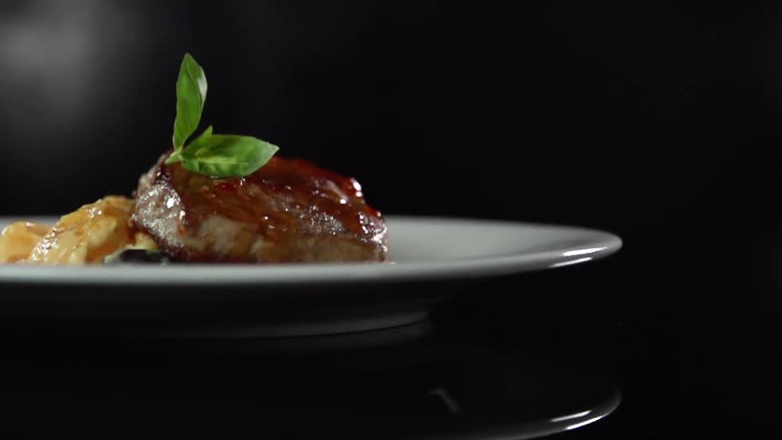 Green garnish falls onto meat on a plate