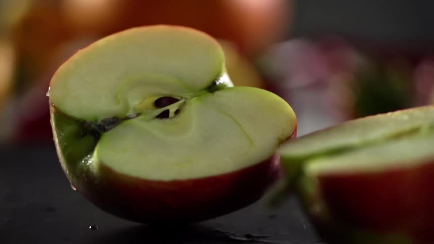 Two halves of a red apple roll on a wooden table