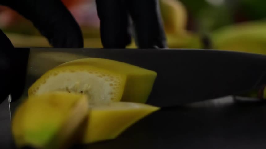 A person uses a sharp knife to slice through an unpeeled banana