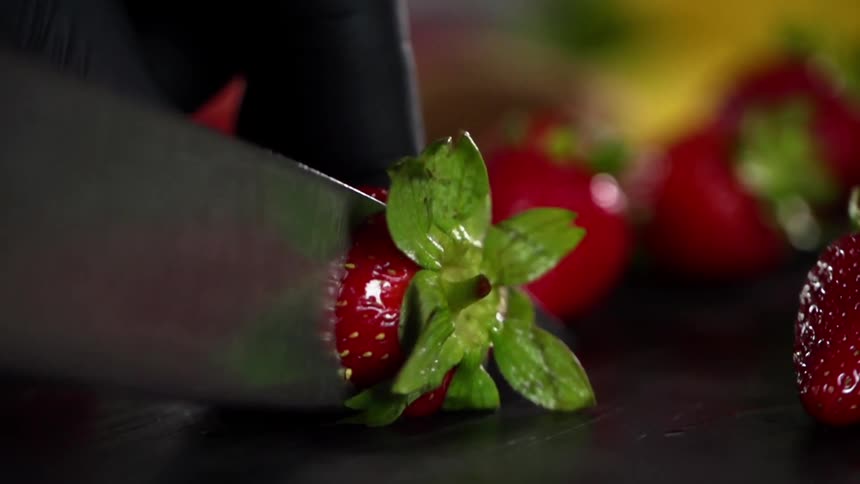 Close up of hands wearing black gloves hulling fresh red strawberries