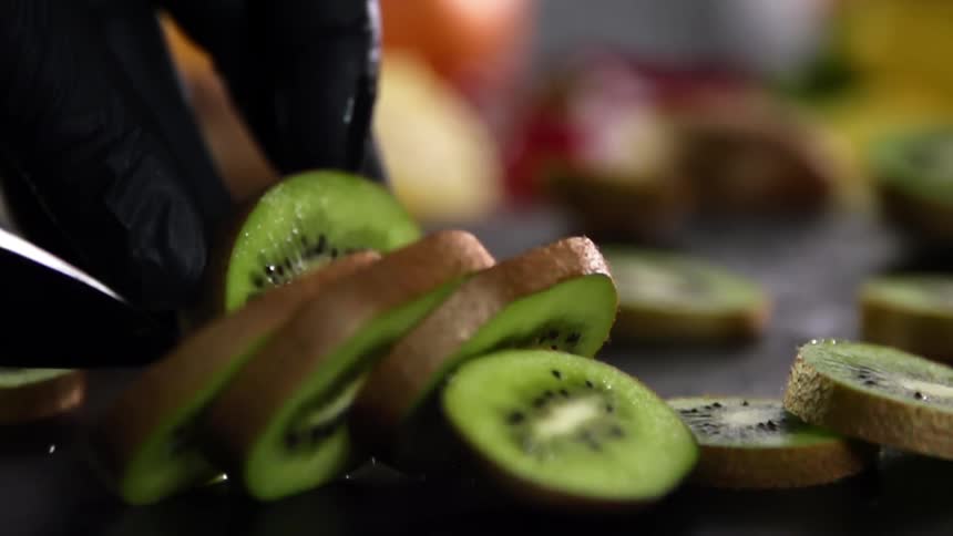 A person cuts slices of kiwi fruit using a sharp kitchen knife