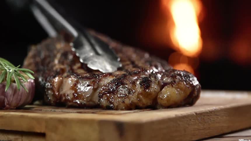 Grilled juicy steak is put on a steak board by a pair of tongs